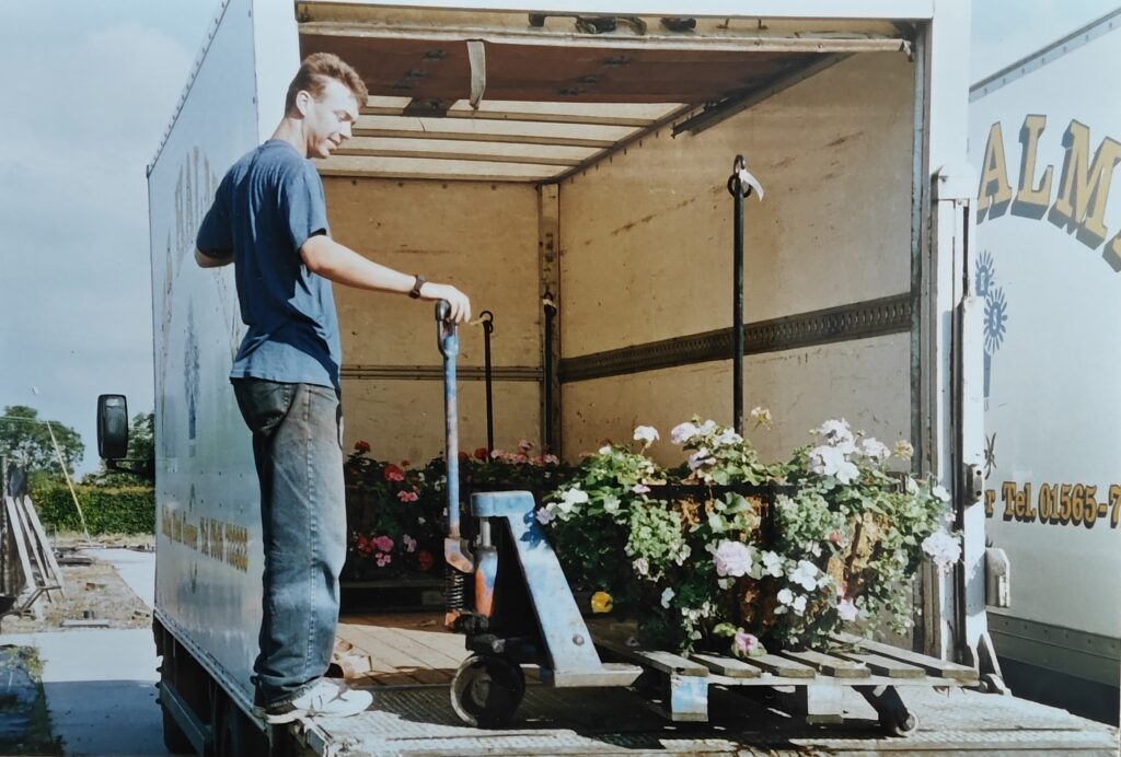 Young man unloading potted plants from a delivery truck at a wholesale plant nursery.